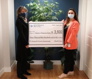 Two women stand on either side of a large check representing the donation LPC is making to the WRC. Both are wearing face masks.